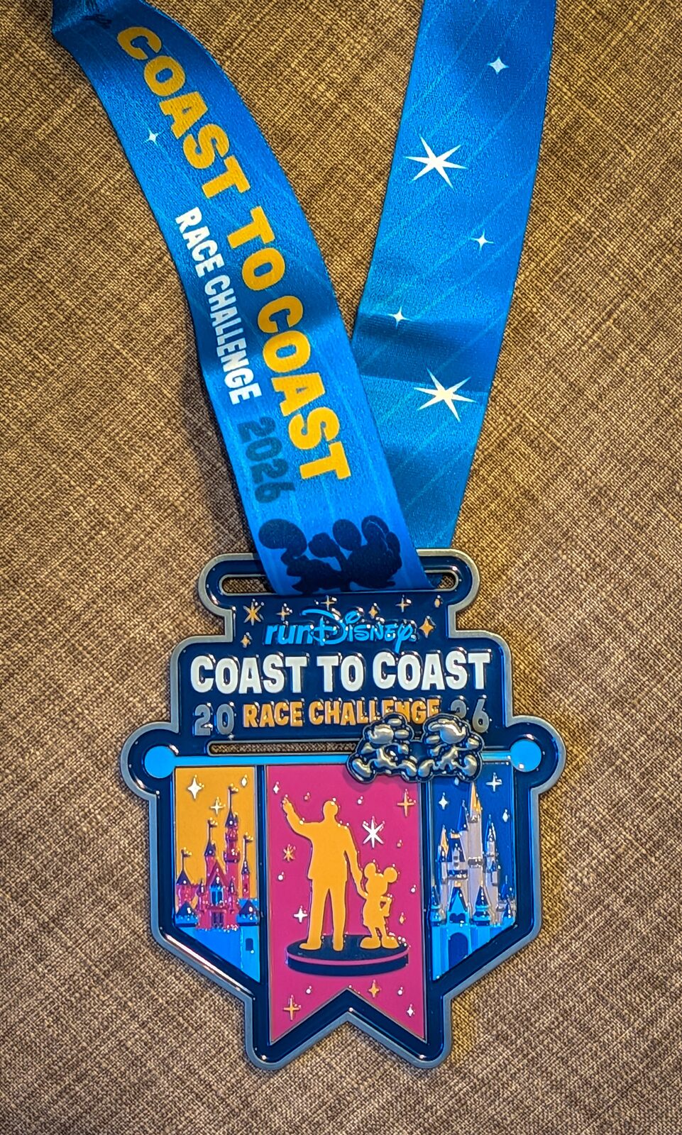 Coast to Coast medal featuring Sleeping Beauty Castle, Cinderella Castle, and the Partners statue silhouette